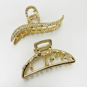 Detail of two gold metal hair claws with textured and smooth liquid designs on white