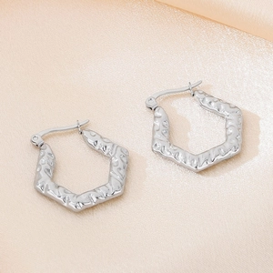 Détail des boucles d'oreilles hexagonales argentées avec texture martelée style lave