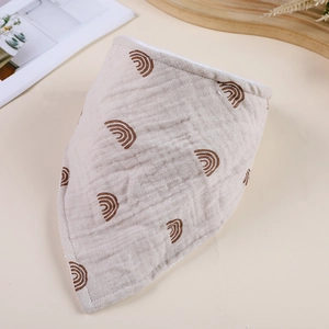 Close-up of beige cotton gauze baby bib with rainbow print on a natural wooden tray