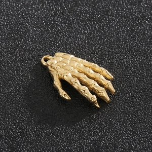 Vintage golden skeleton hand pendant made of stainless steel on a black textured background