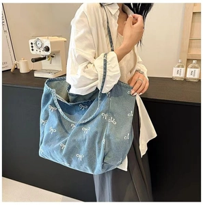 Blue denim tote bag with white bow prints shown on shoulder in a cozy cafe setting