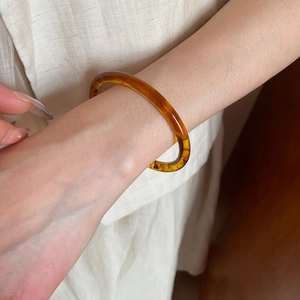 Close-up of translucent amber resin bangle featuring marble textures on a warm fabric background