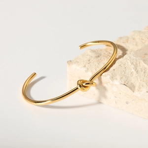 Minimalist knot open bangle in 18K gold plated titanium steel on a natural stone base