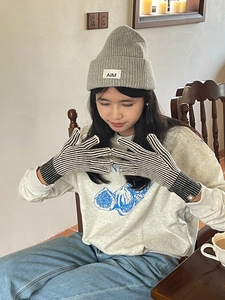 Detalle del gorro de punto gris AIM y guantes de rayas negras y blancas en el modelo