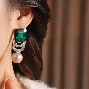 Primo piano di orecchini vintage con gemma verde e perla indossati da una modella