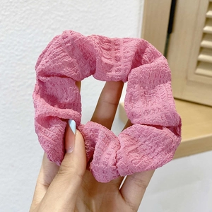 Detailed view of pink pleated scrunchie with soft elastic texture held in hand