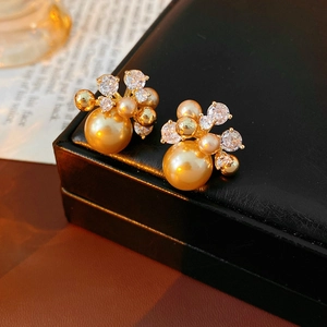 Detailed view of gold pearl earrings with zircon flowers on a black leather box
