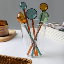 Detail of colorful gradient glass stir spoons in a Good Morning glass cup on a table