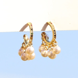 Golden hoop earrings with colorful gemstones and pearl tassels against a blue sky