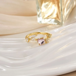 Macro detail of gold ring with pink heart stone and leaf-shaped crystals on white display