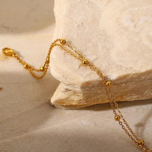 Macro view of double-layer gold bead chain bracelet on minimalist natural stone background