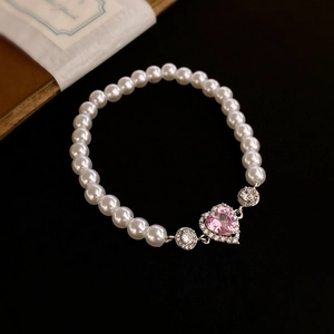 Close-up of pink heart zircon pendant on white pearl bracelet with elegant black background