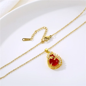 Elegant gold necklace with red teardrop pendant and crystal leaves on white ceramic tray