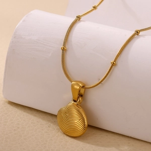 Detail of gold seashell pendant on a beaded snake chain against a neutral background