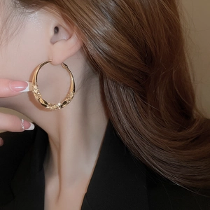Detail of twisted gold hoop earring with hammer-textured finish on a female model