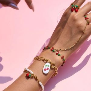 Detailed view of gold chain bracelet with cherry enamel pendant and strawberry pearls