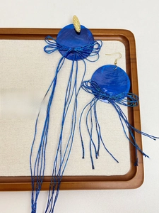 Macro view of blue shell tassel earrings with intricate wire wrapping and bow detail