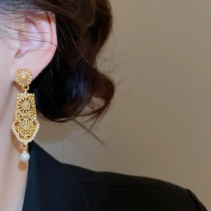 Close-up of geometric gold hollowed earrings with a white pearl drop on model