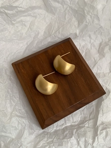 Detailed view of matte gold geometric stud earrings on a minimalist wooden display stand