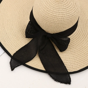 Detail of beige straw sun hat showing fine weave texture and large black mesh bow