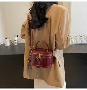 Detail view of burgundy box-shaped handbag featuring gold zippers and premium leather texture
