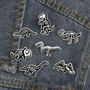 Collection of seven dinosaur skeleton enamel pins pinned on blue denim fabric texture