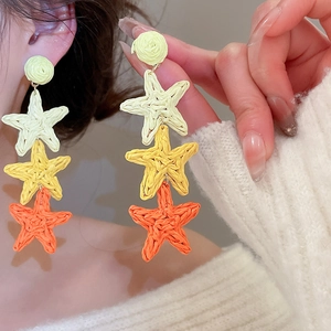 Close-up of three-tier raffia star tassel earrings in yellow, ginger, and orange tones