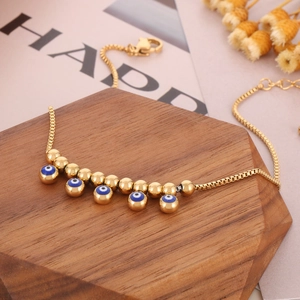 Gold plated evil eye anklet featuring round beads and blue charms on a wood display
