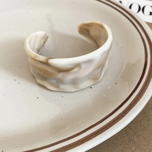 Detail of acrylic open ring with cream marble texture and wavy pattern on ceramic plate