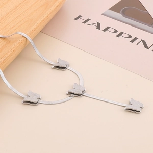 Silver snake chain Y-necklace featuring four matte butterfly charms on a beige surface