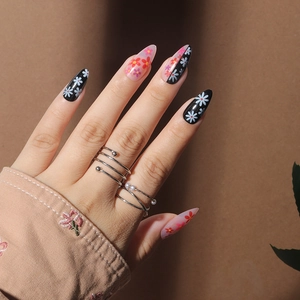Pink and black stiletto press-on nails with floral patterns and pearl rings accessories