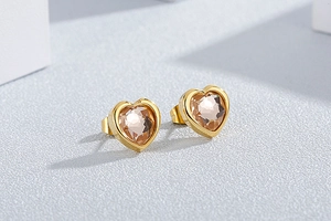Close-up of golden heart earrings with champagne crystal facets on grey background