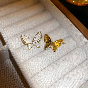Macro detail of gold butterfly earrings with white enamel and sparkling zircon accents