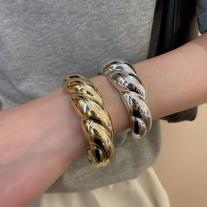 Detail of chunky gold and silver croissant twist bangles on a model's wrist