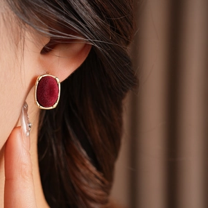 Close-up of golden oval earring with burgundy velvet inlay on a model's ear