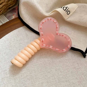 Détail de la pince à cheveux cœur en acrylique rose avec coutures et poignée beige