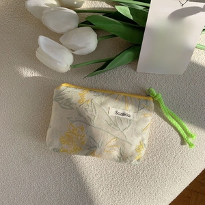 Detail of floral fabric cosmetic bag with yellow zipper and green woven lanyard