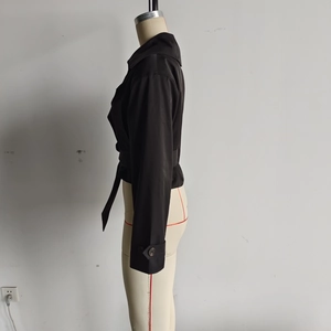 Détail de la veste courte noire avec col à revers et ceinture nouée à la taille