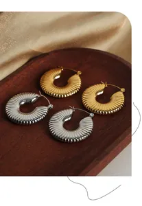 Macro detail of U-shaped gold and silver earrings with radial shell texture on wood tray
