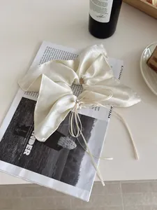 Détail d'un chouchou en satin blanc crème avec perle et strass posé sur un magazine