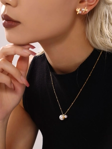 Close-up of gold necklace with white pearls and criss-cross earrings worn by a model