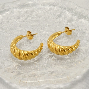 Polished gold stainless steel twisted hoop earrings displayed on a glass tray