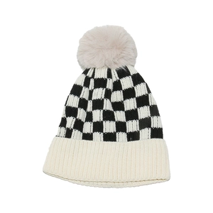 Close-up of black and white checkerboard knit beanie with a soft faux fur pompom on top