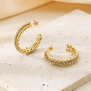 Close-up of golden braided C-hoop earrings with sparkling pavé crystals on stone pedestal