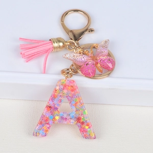 Detail of pink resin letter A keychain with star sequins, tassel and butterfly charm