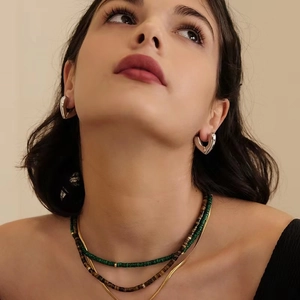 Modern metal heart earrings with layered bead and snake chain necklaces on model