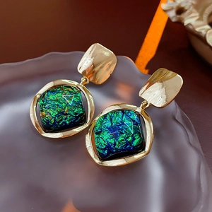 Detailed shot of vintage gold earrings with emerald green resin on frosted glass