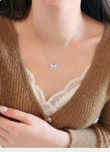 Macro detail of a silver zircon rocking horse pendant worn on a model neckline