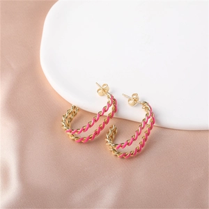Close-up of gold twisted hoop earrings with rose pink enamel finish on champagne silk fabric