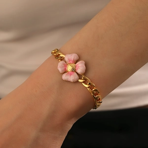 Détail d'un bracelet à breloque fleur dorée porté au poignet avec pétales en émail rose
